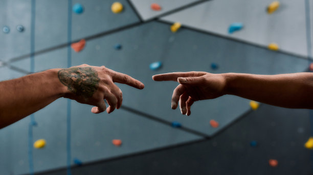 近距离的两个女性和男性的手伸向对方对人工训练攀岩墙。帮助和抱石训练概念图片下载