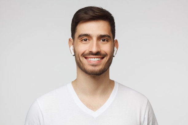 近距离的肖像年轻英俊的微笑的男子穿着白色t恤和无线耳机，享受最喜欢的音乐，孤立在灰色的背景图片下载