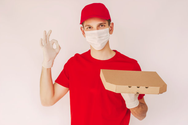 穿着红色制服的快乐快递员，手里拿着披萨盒，露出ok的标志图片下载