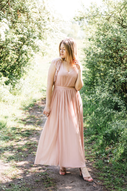 美丽的年轻女子穿着优雅的白色连衣裙站在森林的道路上。漂亮的金发女孩呆在花园里图片下载