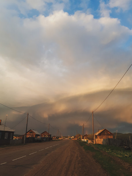 这张照片拍摄的是一个村庄的街道，路上有电线，日落时木头房子的剪影，美丽的蓝天和白色的黄色戏剧性的云图片下载