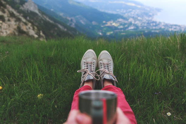 特写照片的杯子与茶在旅行者的手超过聚焦山的观点。一个年轻的女游客喝着一杯热饮，欣赏着山上的风景。徒步旅行的概念。图片下载