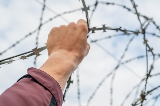 一个男人的手握着铁丝网。逃避的概念图片下载