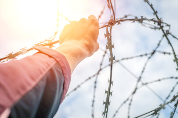 一个男人的手握着铁丝网。逃避的概念。照片与照明，光图片下载