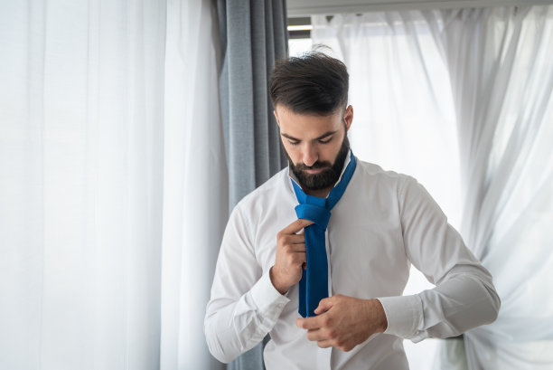 年轻英俊优雅的蓄着胡须的商人穿着衬衫试图在早上去上班之前系上他的领带图片下载