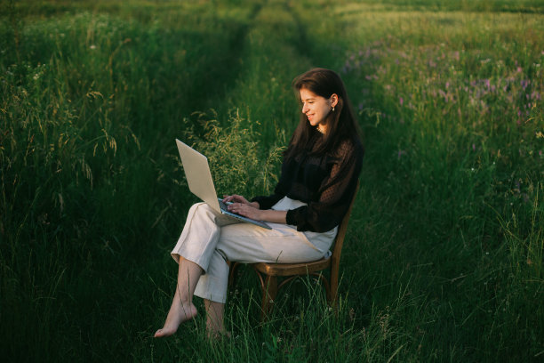 时尚优雅的女孩工作在笔记本电脑上，坐在乡村椅子在绿色的夏日田野。新办公室的概念。有社交距离和安全协议的远程工作图片下载