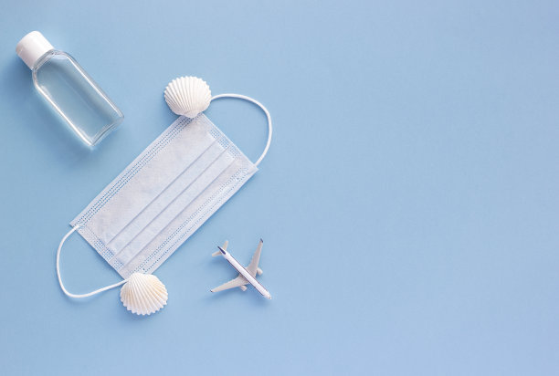俯视图的医疗口罩，飞机模型，消毒凝胶上的蓝色背景与复制空间。在旅行期间预防冠状病毒或COVID-19的概念。平铺，拷贝空间。图片下载