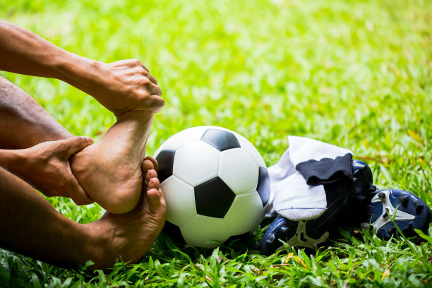 足球和运动鞋在绿色的草地上与足球运动员的脚因为疼痛的脚踝。图片下载