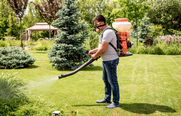 戴着防护面罩和眼镜的园丁向树木喷洒有毒农药图片下载
