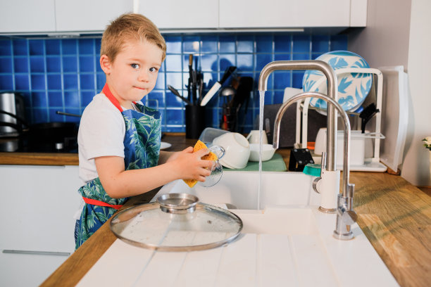 一个穿围裙的男孩在家里的厨房里洗碗图片下载
