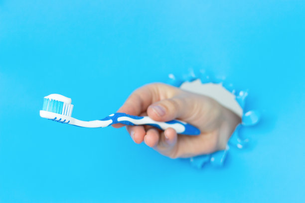 一个女人的手握牙刷与牙膏在蓝色撕破的纸背景图片下载