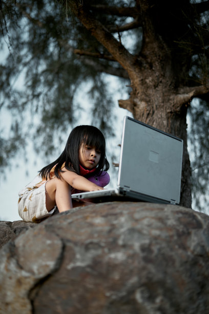 小女孩坐在树下使用笔记本电脑的肖像，教育理念的新常态图片下载