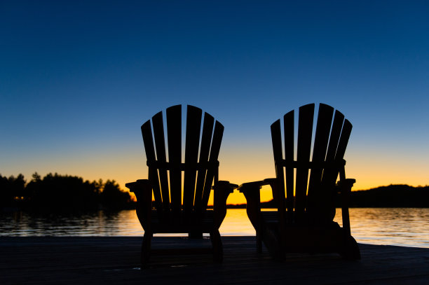 日落时分，两张马斯科卡椅子坐在木屋的木码头上。图片下载