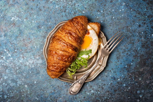 牛角面包三明治，煎蛋和芝麻菜叶在老式银盘子上图片下载