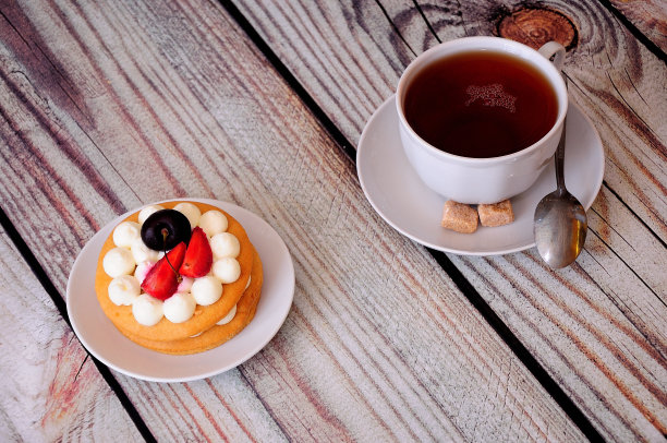 桌上有一杯茶，旁边放着一块奶油、草莓和樱桃的圆饼干蛋糕。图片下载