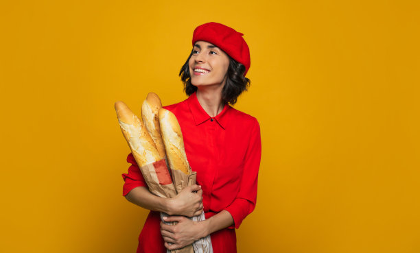 法式面包。一个年轻的法国女人的半腿照片。她穿着巴黎式的红色套装，怀里抱着法式面包，微笑着斜眼看着。图片下载
