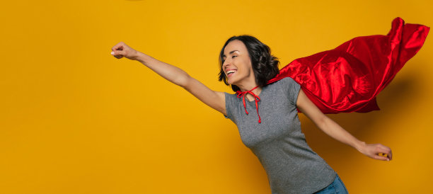 新的冒险!一个年轻美丽的女孩，假装自己是一个女超人，并在一个经典的超人姿势飞行，但与超人红色斗篷，这是在风中谄媚。图片下载