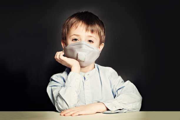 小男生戴着医用防护口罩在教室里以黑板为背景图片下载