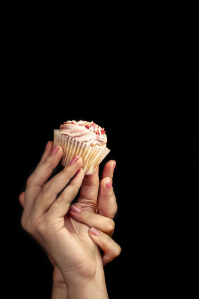 女性的手拿着一个诱人的，美丽的纸杯蛋糕在一个黑色的背景。不健康的甜食观念图片下载