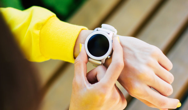 smartwatch。这是一个穿着黄色连帽衫的女孩的特写照片，她戴着一块白色的现代智能手表，用两个手指打开手表。图片下载