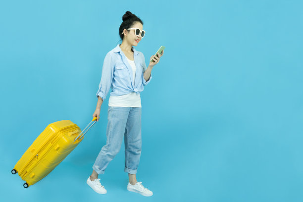 暑假、假期和旅游概念。快乐的旅行者旅游美丽的年轻亚洲女人在休闲衣服和太阳眼镜与黄色手提箱或行李袋孤立在蓝色背景。图片下载