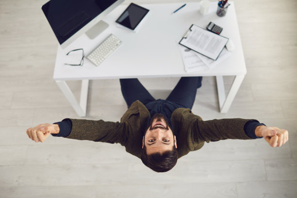 俯视图一个快乐的商人举起他的手在办公室的成功工作。图片下载