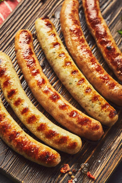 美味的烤猪肉香肠与香料和香草在木砧板上在黑色背景上近距离观看。俯视图，平面布局。图片下载