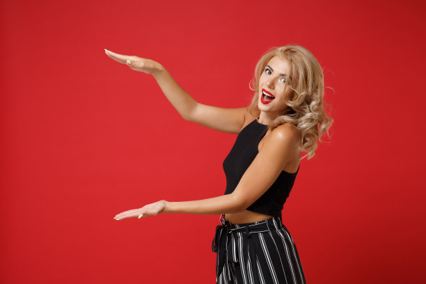 兴奋的年轻女子女孩在黑色衣服摆孤立的红墙背景。人们真诚的情感生活理念。模拟复制空间。手势演示大小与垂直工作空间。图片下载