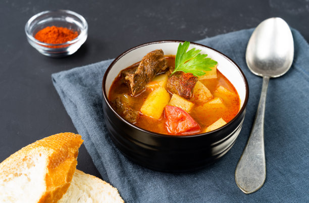 深色盘子里的匈牙利汤，背景色为深色，配以红辣椒。水平方向图片下载