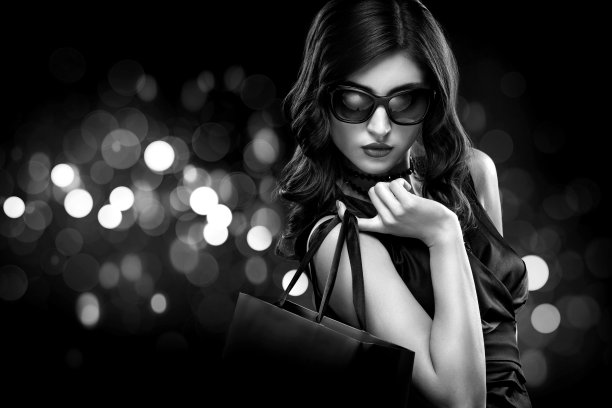 圣诞节或黑色星期五促销概念。购物女人拿着包在黑暗的背景与散景假日。黑白照片。图片下载