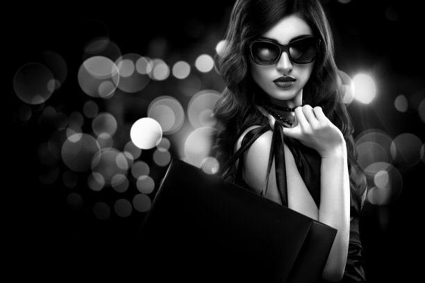 圣诞节或黑色星期五的肮脏概念。购物女人拿着包在黑暗的背景与散景假日。黑白照片。图片下载