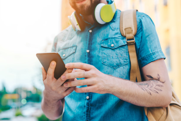 这是一名穿着随意、蓄着胡须的男子背着背包在智能手机上浏览手机应用程序的剪影图片下载