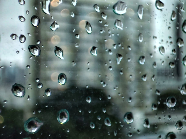 在城市里下雨。水滴落在玻璃上，背景是近景公寓大楼。风暴季节雨量与天气气候变化概念。图片下载