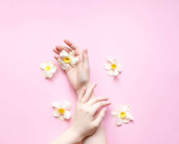 创意美照片手女孩坐在粉红色的桌子。时尚艺术手在春天的时间和花朵在粉红色的背景。护肤概念。图片下载