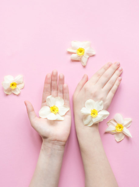 创意美照片手女孩坐在粉红色的桌子。时尚艺术手在春天的时间和花朵在粉红色的背景。护肤概念。图片下载