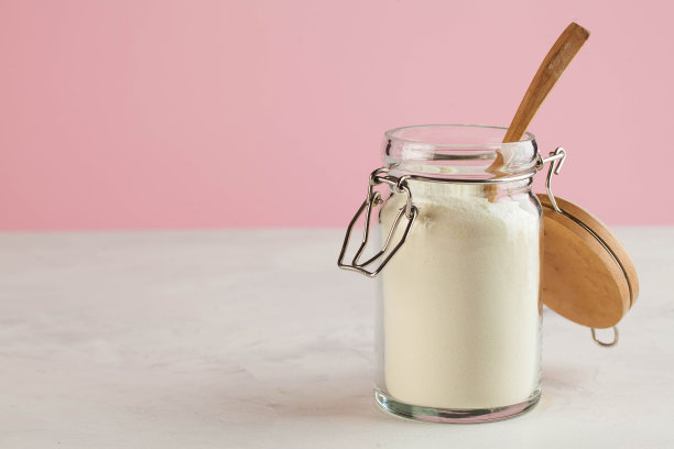 白色胶原蛋白或蛋白粉透明罐，粉色背景上有一个木勺。副本的空间。图片下载