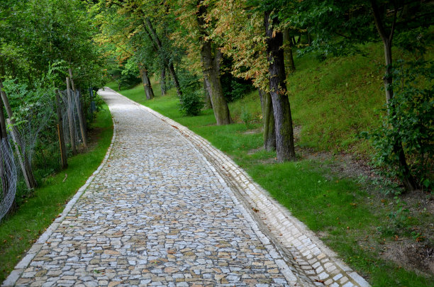 由不规则立方体组成的新公园小径，折叠着一条用于排水的侧通道。花岗岩石头的灰色和棕色的地方，路径是封闭的黑色金属栏杆图片下载