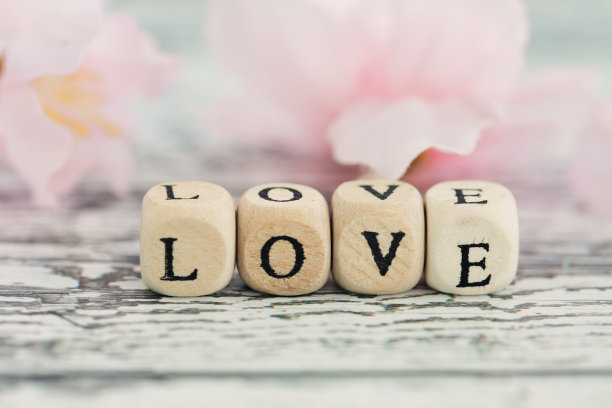 白色木质背景上带有“爱”字的木块，文字“爱”，粉色花朵背景图片下载