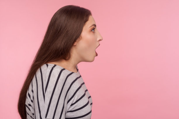 天啊，哇!侧视图惊讶的女人在条纹运动衫站着与张开的嘴，表示惊讶图片下载
