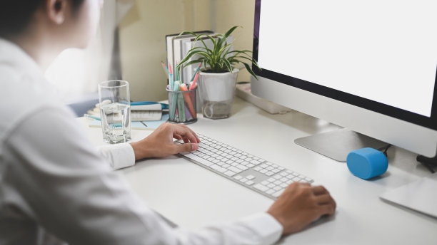 这个办公室职员正在白色的办公桌前用一台白色的黑屏电脑工作。图片下载