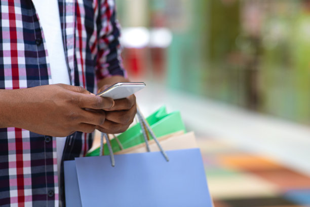 超市夜未眠的概念。拿着购物袋的男人在购物中心使用智能手机图片下载