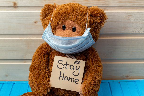 带着字的泰迪熊呆在家里，戴着医用防护口罩在木制的背景上图片下载