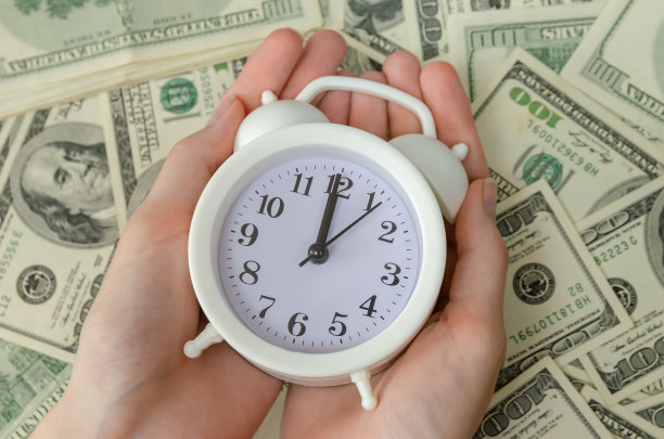 女人的手与一个白色的闹钟躺在美元的背景特写。金融、商业概念图片下载