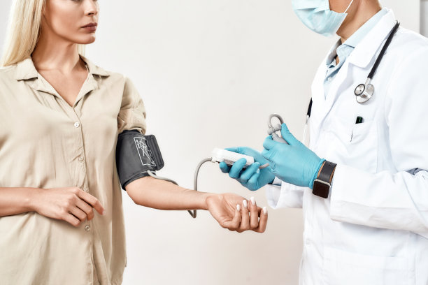 男医生身着医疗制服，佩戴防护面罩和蓝色无菌手套测量年轻女性、女性患者的血压图片下载