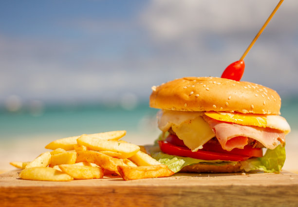 汉堡配芝士、蔬菜、火腿、薯条，背景是大海图片下载