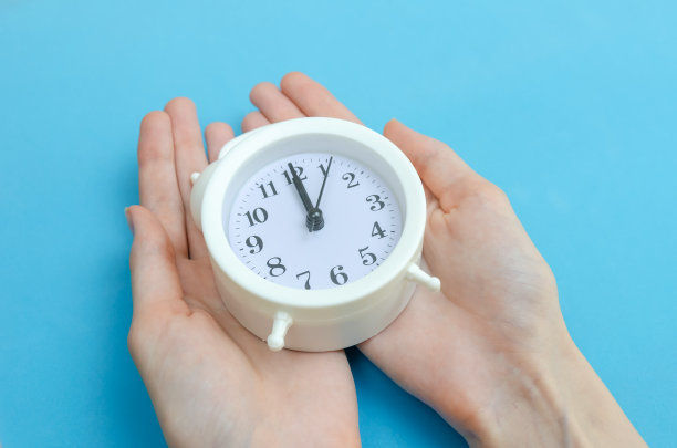 女性手中拿着一个蓝色背景的白色闹钟，复制空间。图片下载