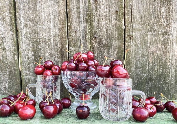 大的成熟的红色樱桃在一个抽象的木制表面的背景玻璃容器。图片下载