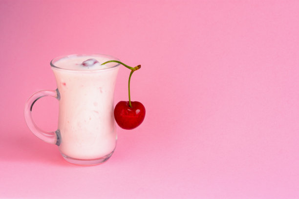 粉色背景的樱桃酸奶杯。一种美味的含樱桃的牛奶饮料。图片下载
