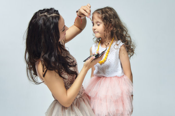 妈妈给她的小女儿化妆。在工作室拍摄白色背景的照片图片下载