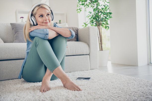 感觉年轻的中年家庭妇女的照片坐在舒适的地板沙发电话躺地毯听音乐现代科技耳机，梦想家呆在家隔离周末客厅室内图片下载